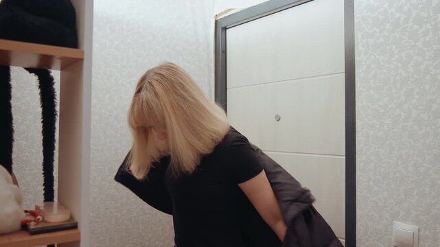 Young white woman putting on coat near apartment door, slipping into puffer jacket, checking pockets, zipping up, gazing down, commuter returning from work, student grabbing keys, subdued filmic