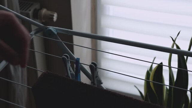 Close-up of a male hand moving colorful clothespins on an indoor clothes drying rack