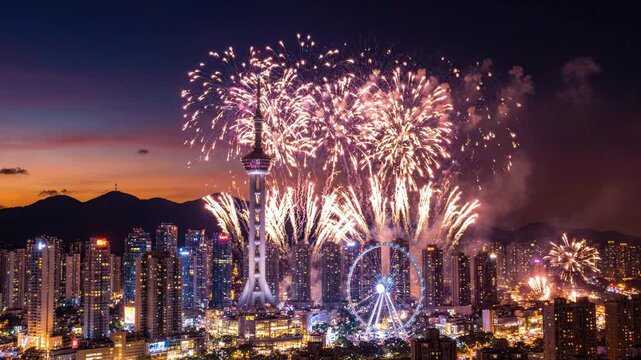 Vibrant fireworks display over cityscape with tower and ferris wheel at dusk with mountains in background