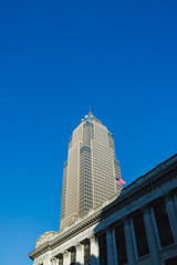 Naklejka premium Tall building stands against clear blue sky in downtown area during afternoon hours with old architecture nearby