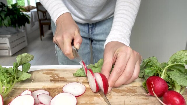 Hands slicing fresh red radishes on a wooden cutting board with a knife. Symbolizes healthy food preparation. Ideal for nutrition, vegan lifestyle, and culinary content. Bright, clean kitchen scene