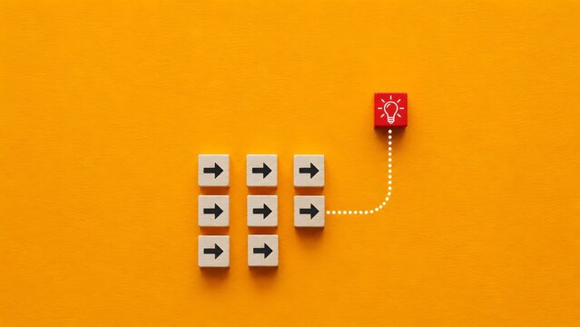 Red lightbulb block breaking away from group of arrow blocks on yellow background symbolizing disruption and thinking differently
