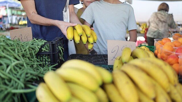Family shopping for fresh, organic bananas and green beans at a vibrant local farmers market, promoting healthy eating and sustainable consumerism