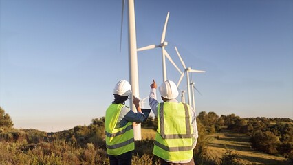 Renewable energy engineers planning wind farm development, discussing sustainable clean power generation while surveying turbines in a natural landscape setting © NJF