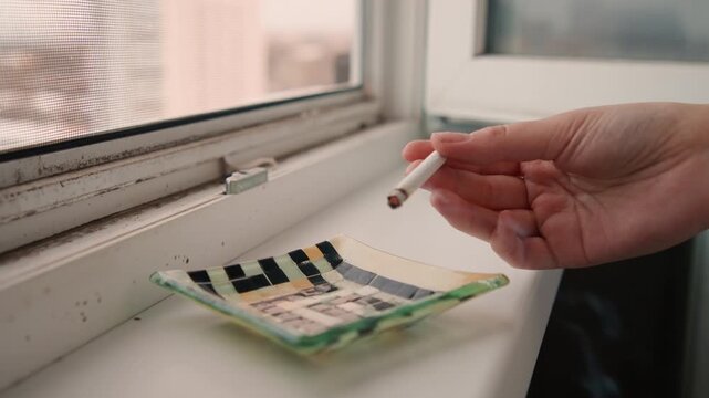 Contemplative artist takes peaceful smoking break. Studio creator steps away to enjoy calm cigarette smoke. Person with hand holding cigarette relaxes near ashtray during thoughtful artistic pause