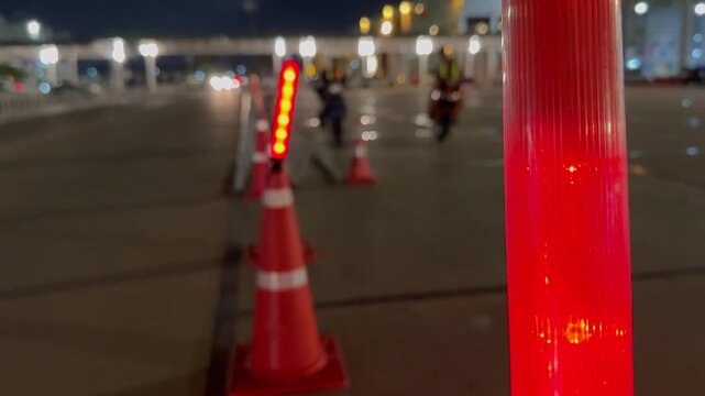 Flashing red neon guiding lights and orange cones on the road, focus of red warning light nighttime traffic control with blurred background.