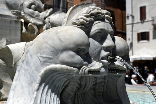 carved stone sculpture, water spout, fountain and scupper. public square in Rome, Italy. bright summer day. blurred  restaurant terraces around. elegant artistic carving. art, travel, tourism concept
