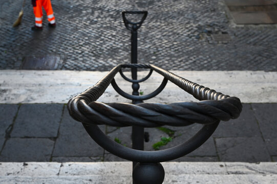 old exterior cobble stone stair in central Rome. twisted  bent double railing on vertical posts. worker in orange work suit sweeping the pavement. travel and tourism concept