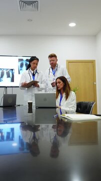 Group of diverse doctors discussing patient diagnosis using a laptop in a modern hospital meeting room. Medical staff analyzing chest x rays