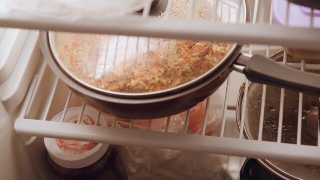 Pan cooling observable. Lidcovered vessel rests on cooling surface. Dish with lid sits on fridge shelf cooling down. Pot covered with lid placed on refrigerator shelf to cool after cooking