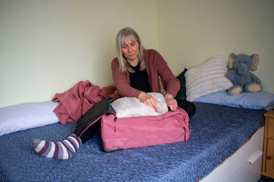 Senior woman placing pillow into suitcase while packing for travel