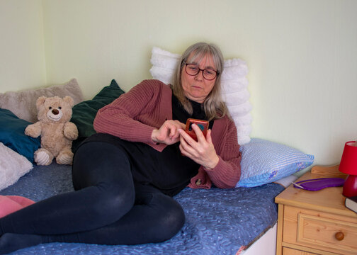 Senior woman using smartphone with serious expression lying on bed at home