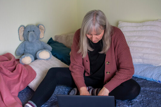 Senior woman using laptop lying on bed focused on screen at home