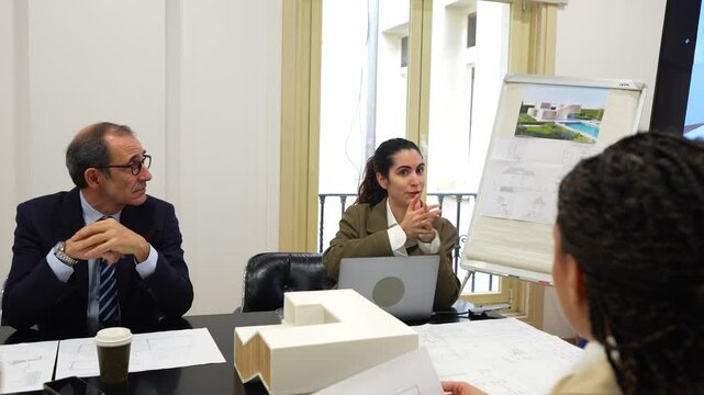 Professional architect presenting a new building project to investors. Colleagues discussing blueprints and looking at a scale model