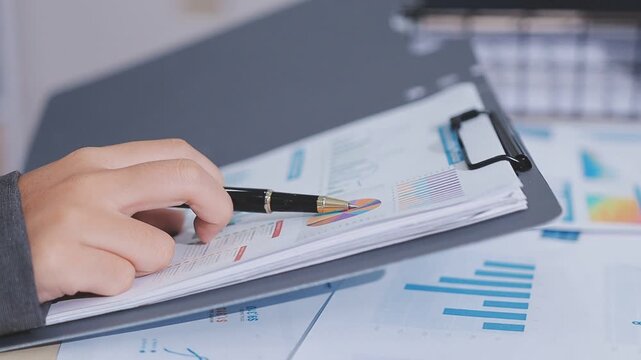 Two accountants examining financial documents using a calculator, taking notes, and discussing results, surrounded by documents and technology in a busy office environment. Audit and taxes in business