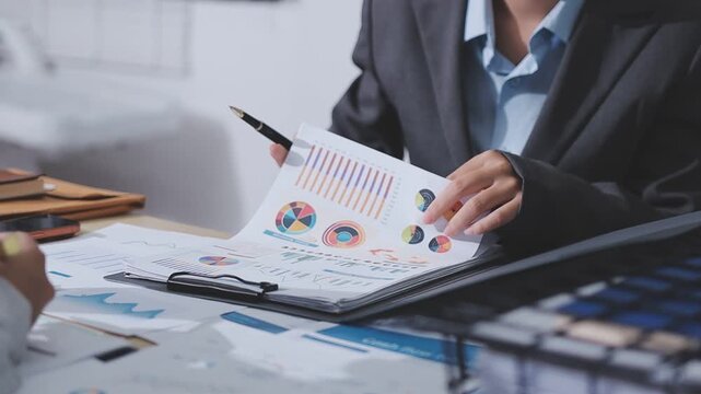 Two accountants examining financial documents using a calculator, taking notes, and discussing results, surrounded by documents and technology in a busy office environment. Audit and taxes in business