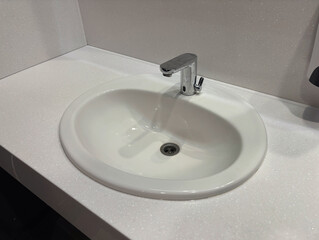 Fototapeta premium Modern white vanity unit with a ceramic sink and faucet in a public restroom or office bathroom