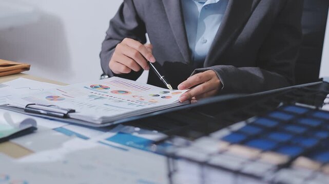Two accountants examining financial documents using a calculator, taking notes, and discussing results, surrounded by documents and technology in a busy office environment. Audit and taxes in business