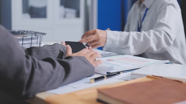 Two accountants examining financial documents using a calculator, taking notes, and discussing results, surrounded by documents and technology in a busy office environment. Audit and taxes in business