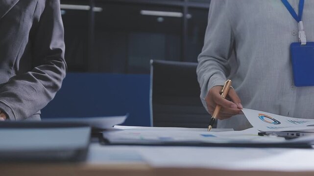 Two accountants examining financial documents using a calculator, taking notes, and discussing results, surrounded by documents and technology in a busy office environment. Audit and taxes in business