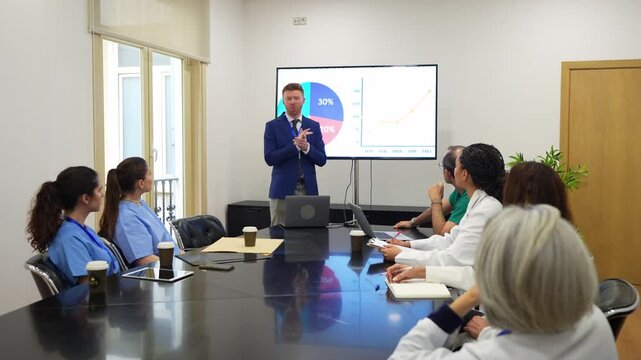 Professional business manager presenting a slideshow with charts and graphs to a team of doctors and nurses in a hospital board meeting