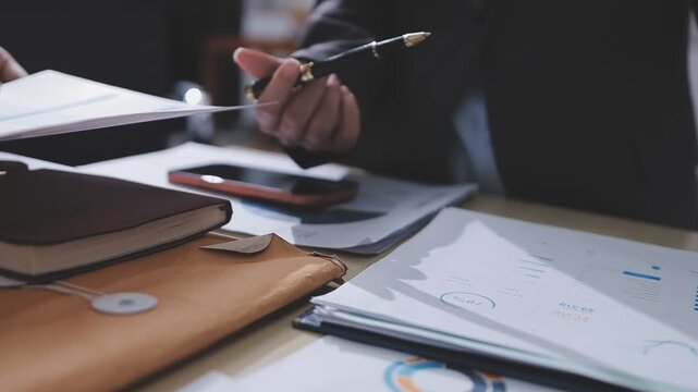Two accountants examining financial documents using a calculator, taking notes, and discussing results, surrounded by documents and technology in a busy office environment. Audit and taxes in business