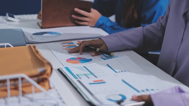 Two accountants examining financial documents using a calculator, taking notes, and discussing results, surrounded by documents and technology in a busy office environment. Audit and taxes in business