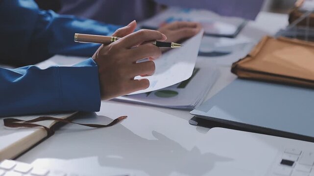Two accountants examining financial documents using a calculator, taking notes, and discussing results, surrounded by documents and technology in a busy office environment. Audit and taxes in business