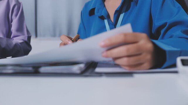 Two accountants examining financial documents using a calculator, taking notes, and discussing results, surrounded by documents and technology in a busy office environment. Audit and taxes in business