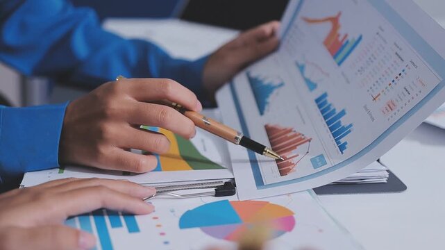 Two accountants examining financial documents using a calculator, taking notes, and discussing results, surrounded by documents and technology in a busy office environment. Audit and taxes in business