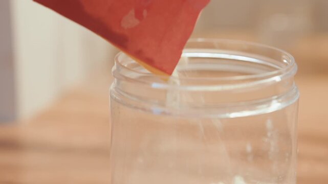 Closeup red bag tipping flour into glass jar for baking, professional baker measurement and precision, scale and technique vibe, controlled pour on countertop, crisp detail and warm studio light