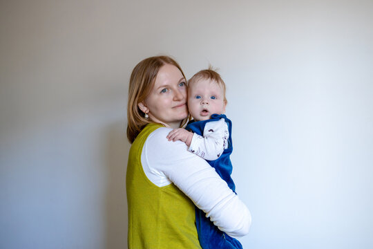 Portrait of a happy young mother gently holding her adorable baby son. They are standing against a neutral light background with plenty of copy space for text. This authentic lifestyle shot captures a