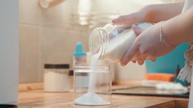 Home baker carefully adds sugar to jar. Precise motion captures sugar pouring into glass jar during morning. Warm morning light highlights baker skillfully measuring and pouring sugar into jar