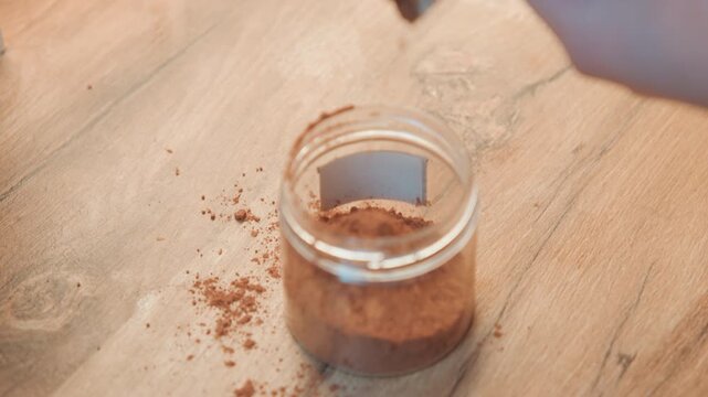 Rustic kitchen scene with sweet seasoning process. Hands sprinkling brown sugar onto jar on wooden surface. Culinary scene showing pastry chef applying sugar topping in rustic kitchen setting