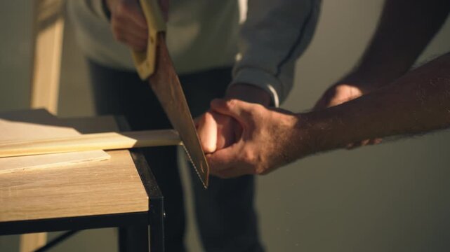 Close-up of father and son sawing wooden plank together during DIY home improvement project, focusing on teamwork, construction work, and hands-on building activity.