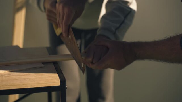 Close-up of father and teenage son working together with a hand saw, as father carefully guides son&rsquo;s hands, teaching patience, safety, and practical woodworking skills.