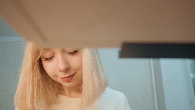 White woman checking oven during cooking, blonde hair and focused expression, warm kitchen lighting, closeup under range hood, domestic meal preparation, quiet morning routine, home cook perspective