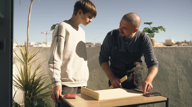 Father helping teenage son measure and cut wooden board for school DIY project, demonstrating practical skills, learning, and educational hands-on activity.