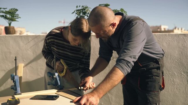 Father and teenage daughter working together on outdoor DIY home improvement project, sawing wooden plank for practical construction task.