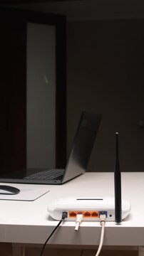 Vertical video hand holding scissors cutting a gray network cable plugged into a white modem router on a clean desk, symbolizing disconnection