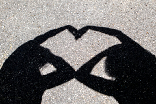 Shadow heart made by two people forming a love gesture with hands on sunlit pavement