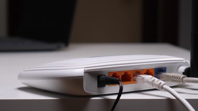 Person's hands connecting a white ethernet cable into the lan port of a white wireless router, setting up internet connection and network connectivity on a modern desktop