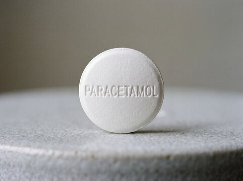 A professional photography close-up shot of a white round pill with the word PARACETAMOL clearly debossed on its surface, resting on a clean neutral background.