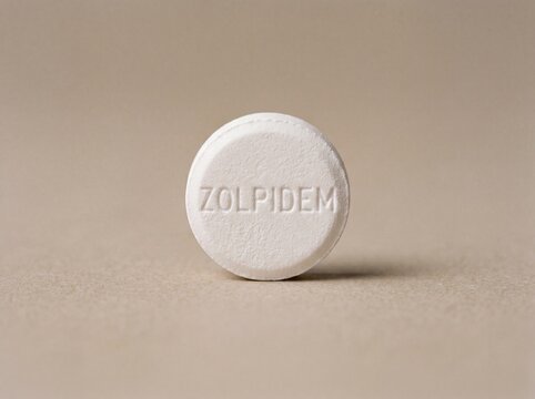 A professional photography close-up shot of a small circular tablet with ZOLPIDEM engraved on the surface, set against a smooth neutral background.