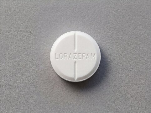 A professional photography close-up shot of a scored round white pill with LORAZEPAM legibly debossed, resting on a solid neutral background.