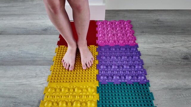 In horizontal slow-motion video, a child steps onto colorful rubber massage mats, engaging in autonomous foot care exercises to prevent common pediatric foot issues. Early intervention program clips