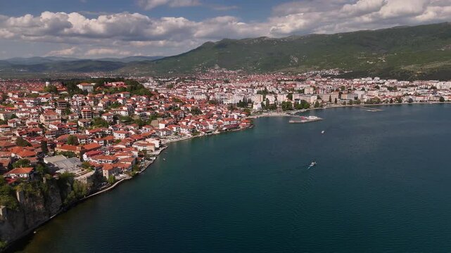 4K drone slow pan over Ohrid city coast showing old town rooftops and a boat cruising Lake Ohrid, North Macedonia