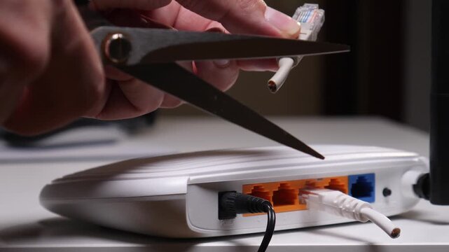Hand holding scissors and cutting an ethernet cable connected to a white wireless router, symbolizing disconnection, digital detox, or censorship from online world