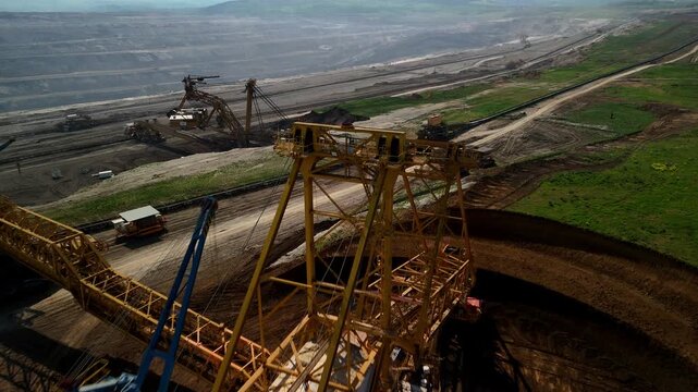 Horizontal drone flyover above a bucket wheel excavator, gradually revealing additional mining machines and the vast open pit quarry landscape beyond.
