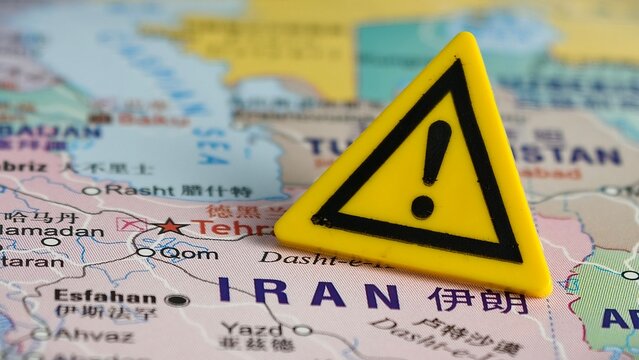 A yellow warning sign with an exclamation mark is placed over a map of Iran, highlighting regional conflict, travel alerts, or geopolitical risk.